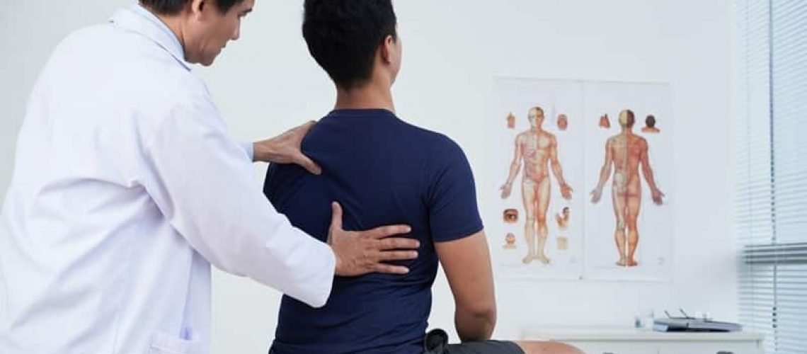 Doctor checking spine of a young man within the annual medical examination